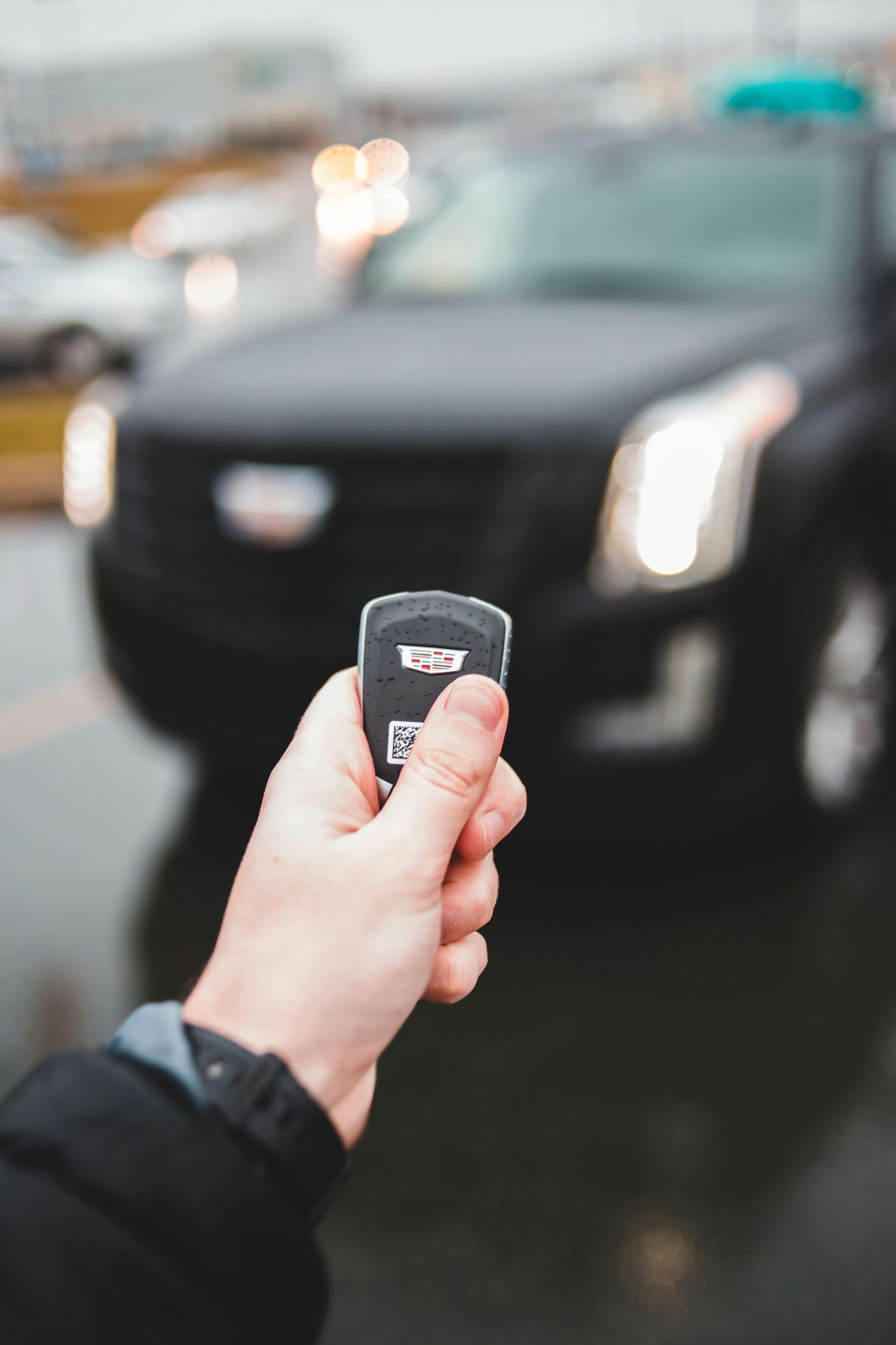 A person is holding a remote control in front of a car.