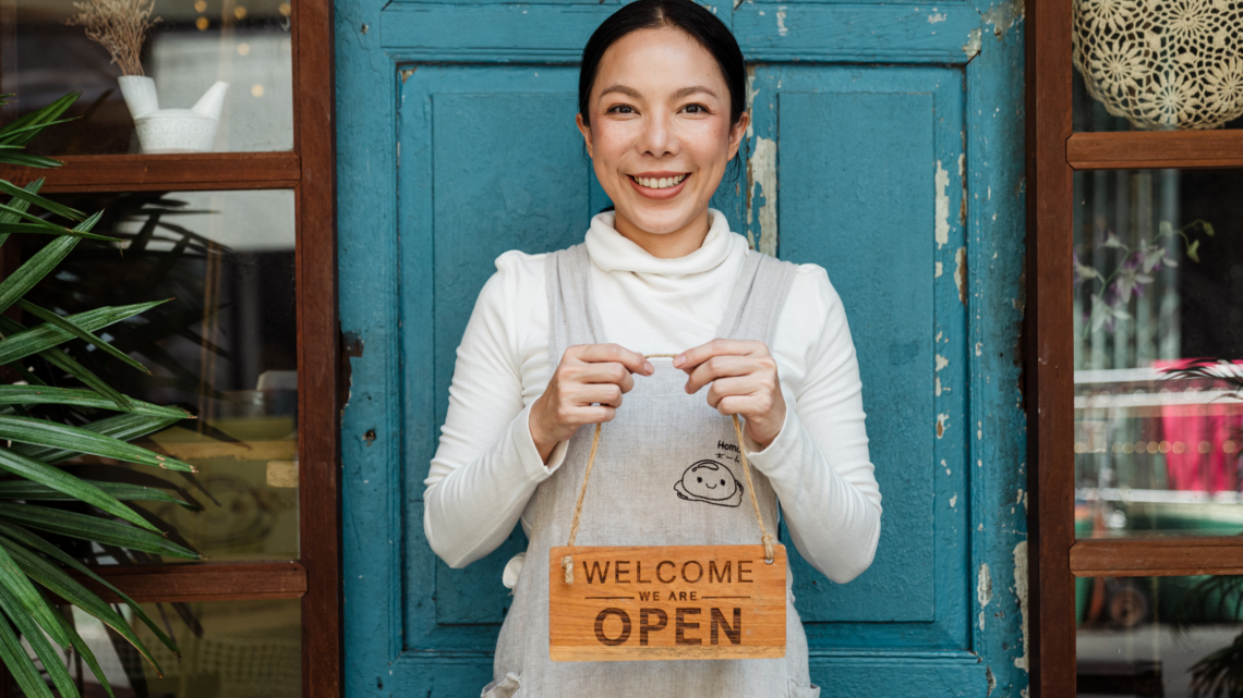 A woman is standing in front of a blue door holding a welcome sign.