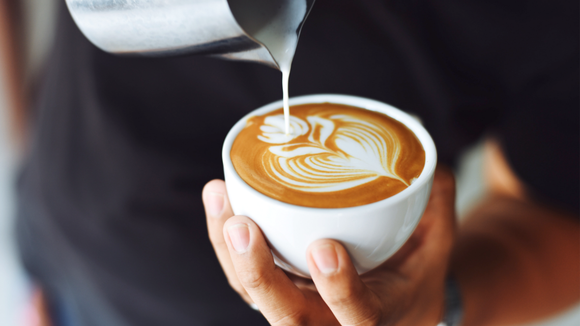 A person is pouring milk into a cup of cappuccino.