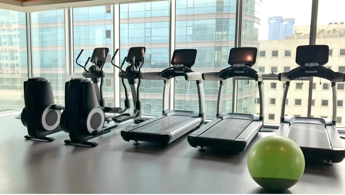 A gym with treadmills , ellipticals , and a green ball.