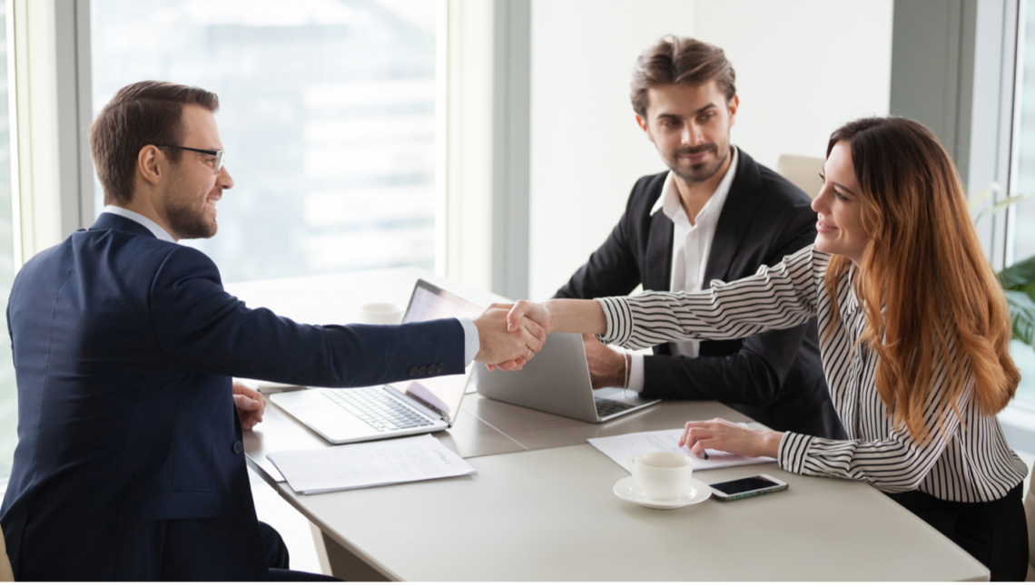 A man and a woman are shaking hands while sitting at a table.