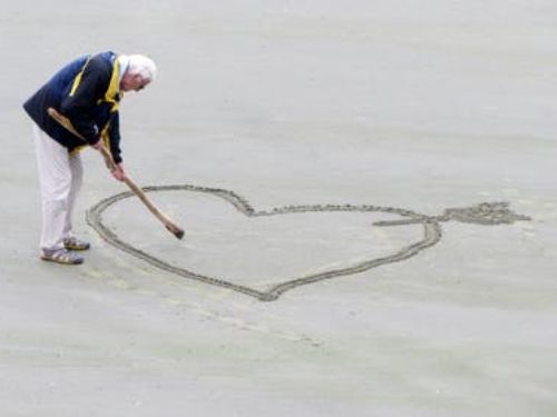 A man is drawing a heart in the sand enjoying his retirement.