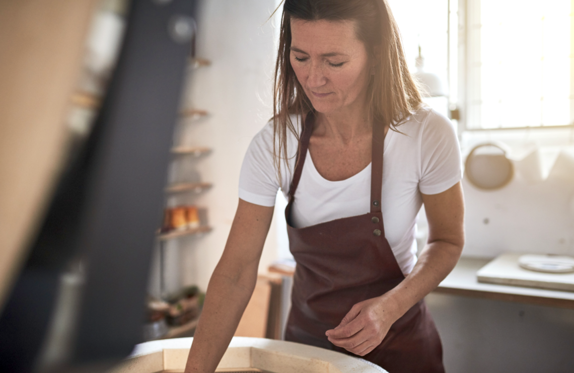 A woman in an apron is standing next to a large bowl in a kitchen.