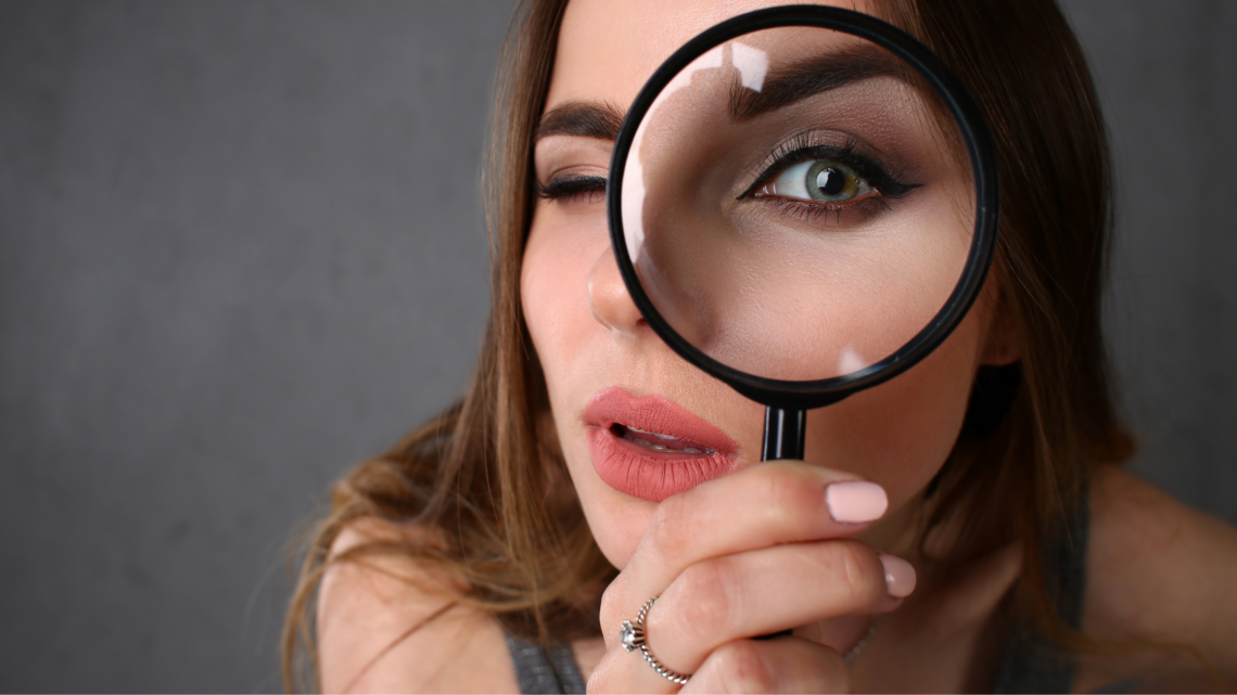 A woman is looking through a magnifying glass at her face.