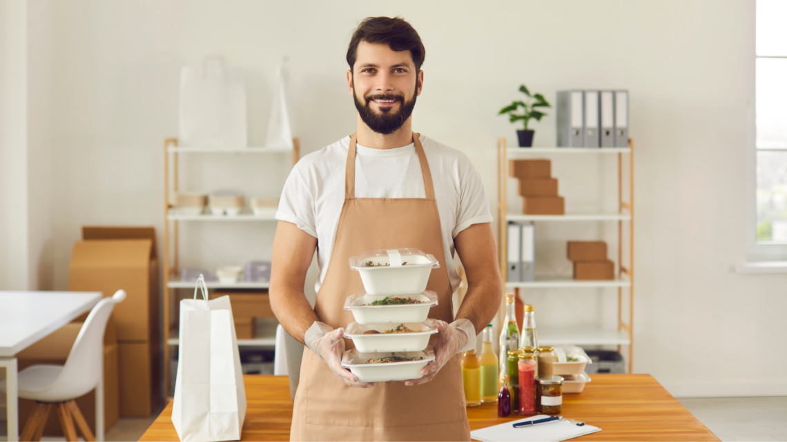 A man in an apron is holding a stack of plastic containers.