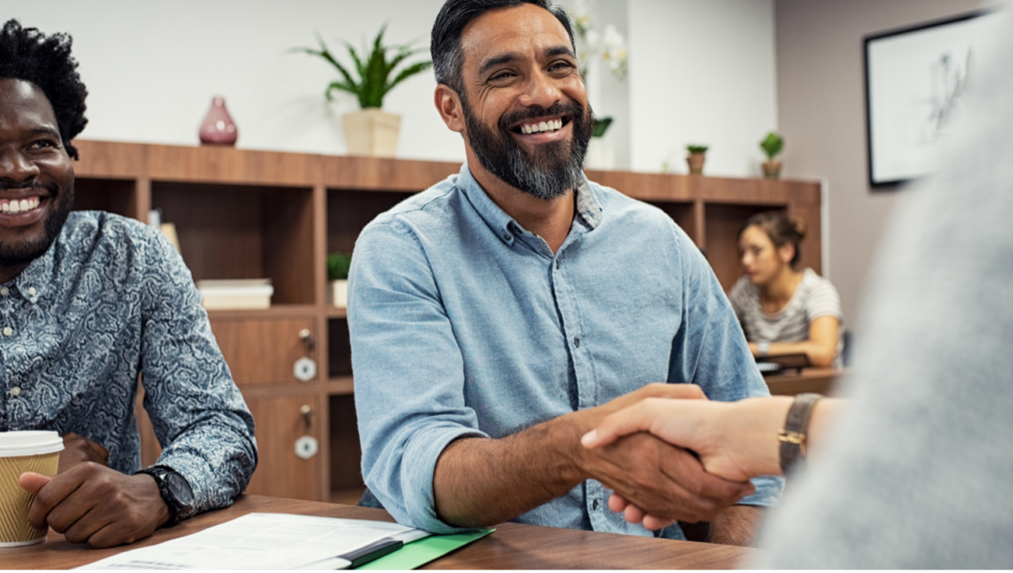 A man is shaking hands with another man while sitting at a table.