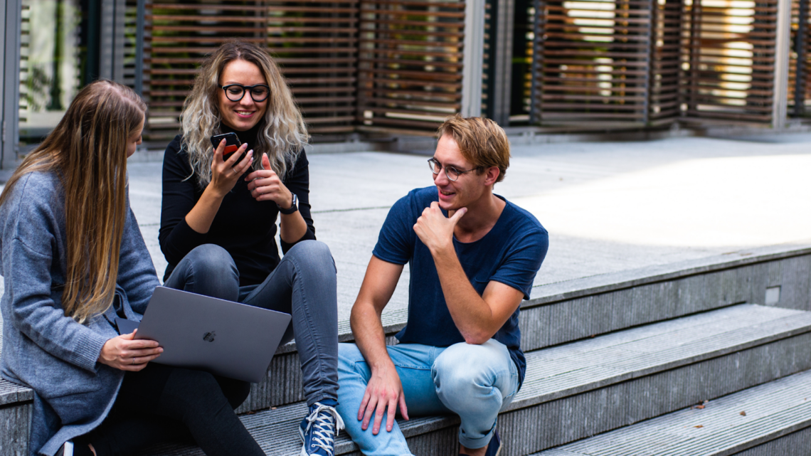 A group of people are sitting on the steps of a building talking to each other.