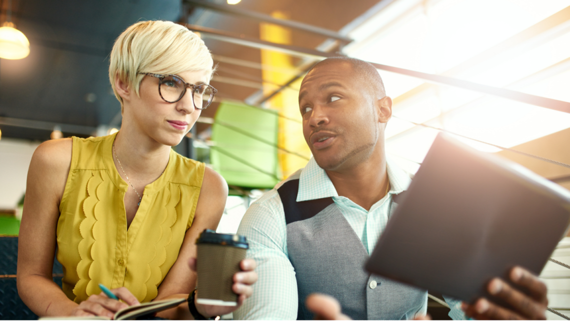 A man and a woman are sitting at a table looking at a tablet.