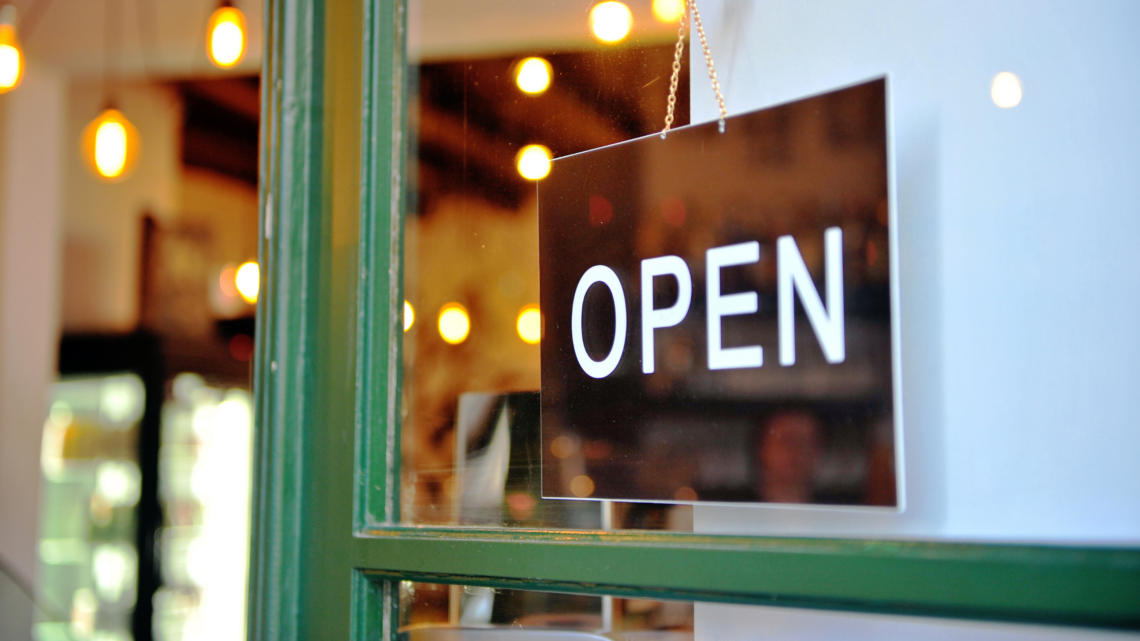 A black and white open sign is hanging on a green door.