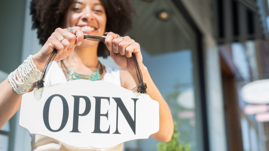 A woman is holding an open sign in front of a store.