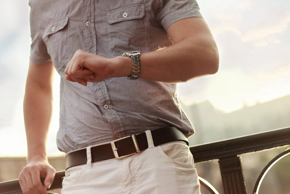 A man is standing on a balcony looking at his watch.
