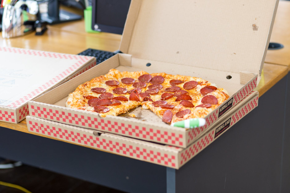 A pepperoni pizza in a cardboard box on a desk.