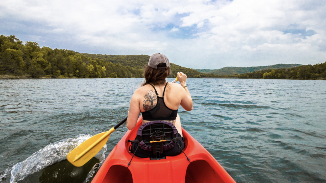 A woman is paddling a red kayak on a lake.