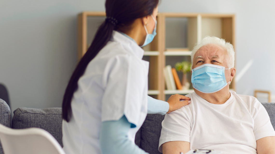 A nurse is talking to an elderly man wearing a mask.