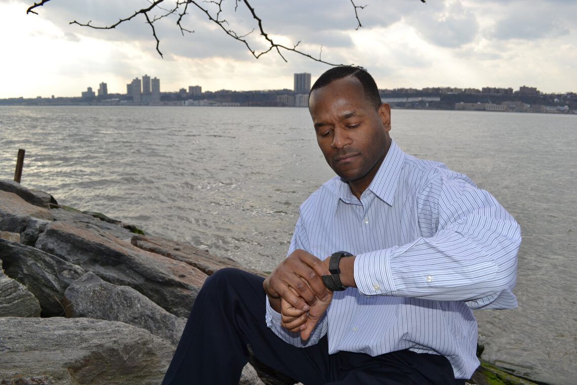 A man sits on a rock near the water looking at his watch