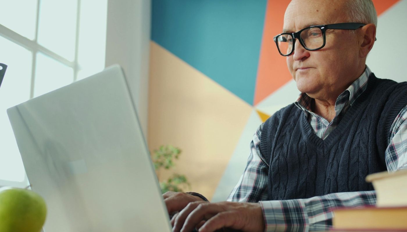 A senior man working on a computer while reflecting on fears about buying a franchise.