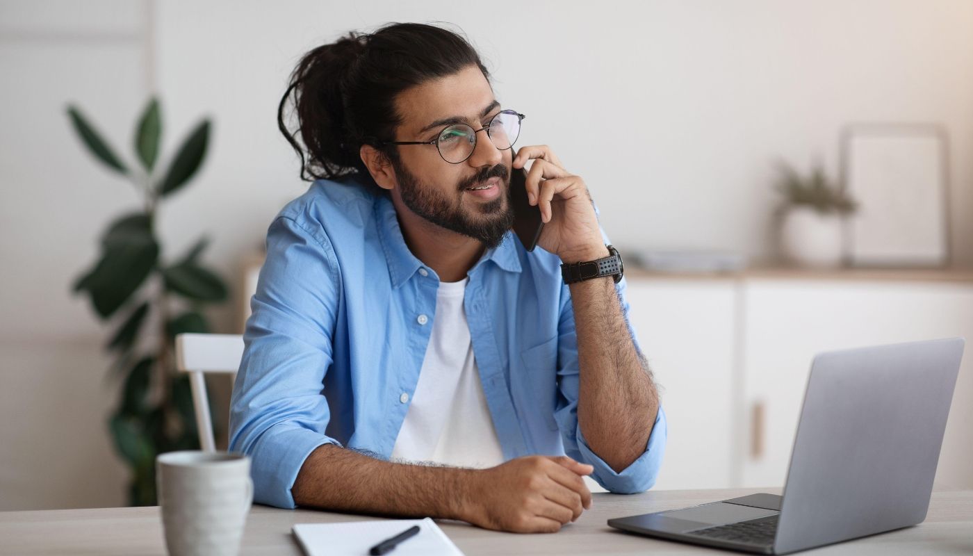 Man talking on the phone and using a laptop to find franchise financing options.

