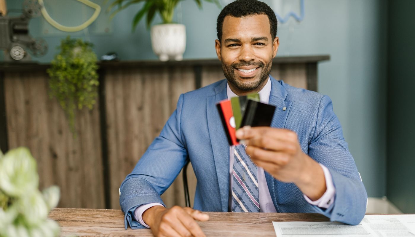 Smiling businessman in a suit holding credit cards at a business desk while reviewing franchise financing options.