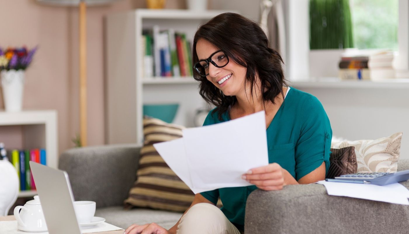 Woman holding financial papers and using a laptop to estimate franchise startup costs and plan her investment. 
