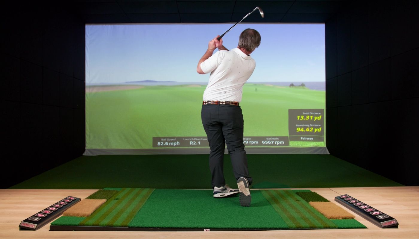 Adult man playing a game indoors in a golf simulator franchise.