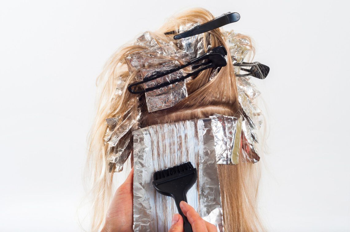 A woman is getting her hair dyed with a brush and foil.