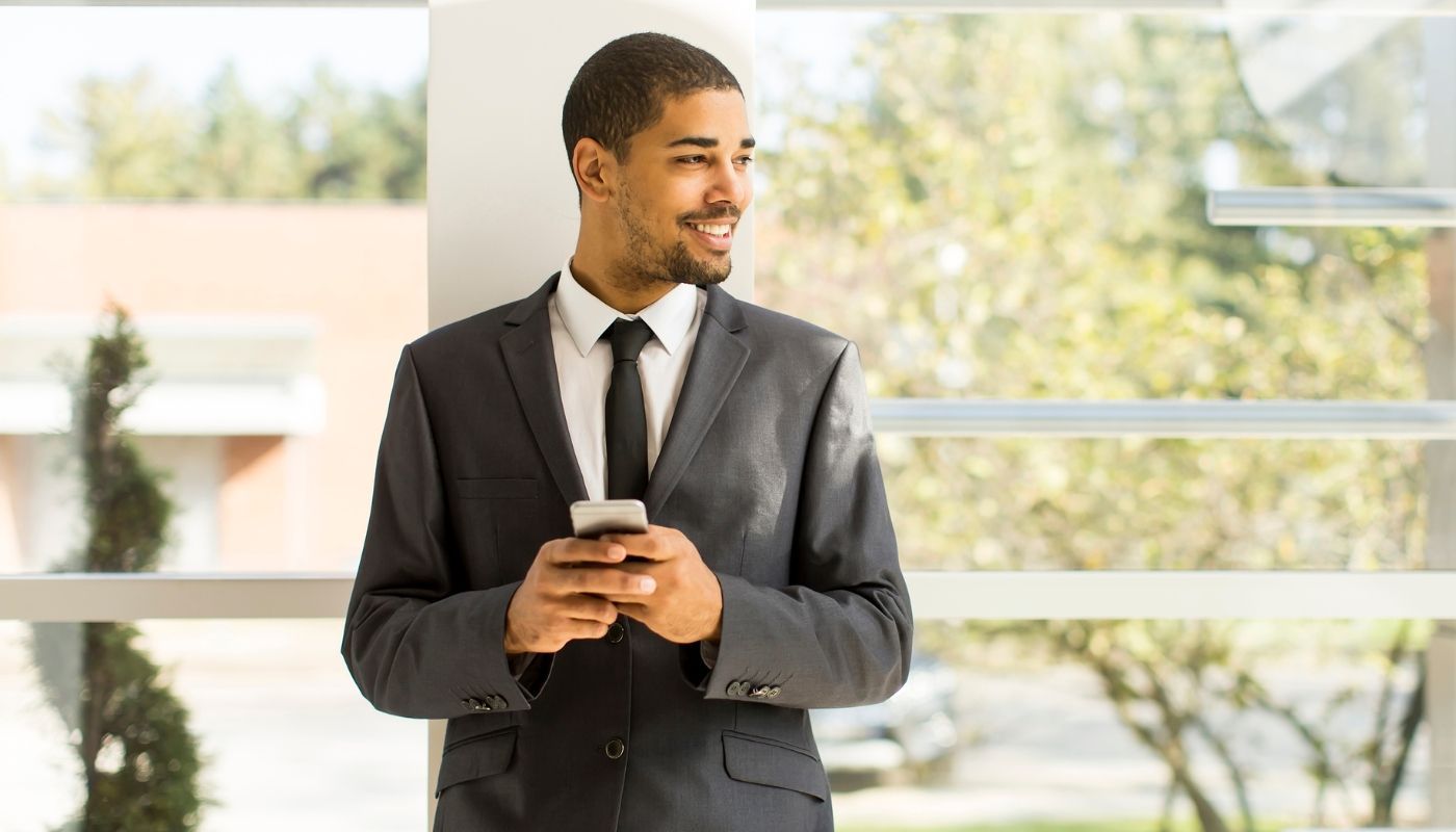A young entrepreneur with a phone smiling in his franchise office.