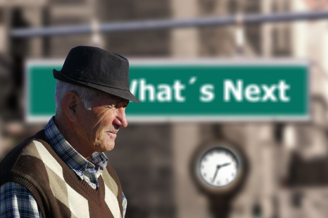 A man wearing a hat stands in front of a sign that says 