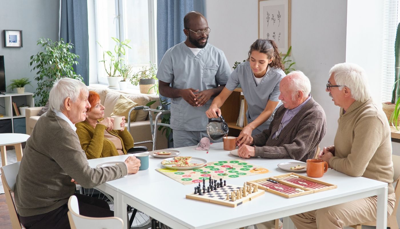 A nurse pouring tea for a couple of seniors enjoying board games owning a senior care franchise