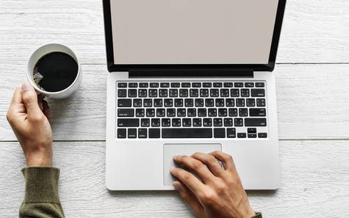 A person is typing on a laptop computer while holding a cup of coffee.