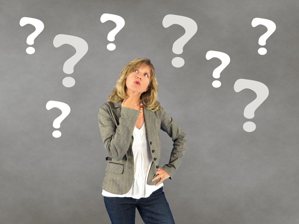 A woman is standing in front of a wall with question marks painted on it.