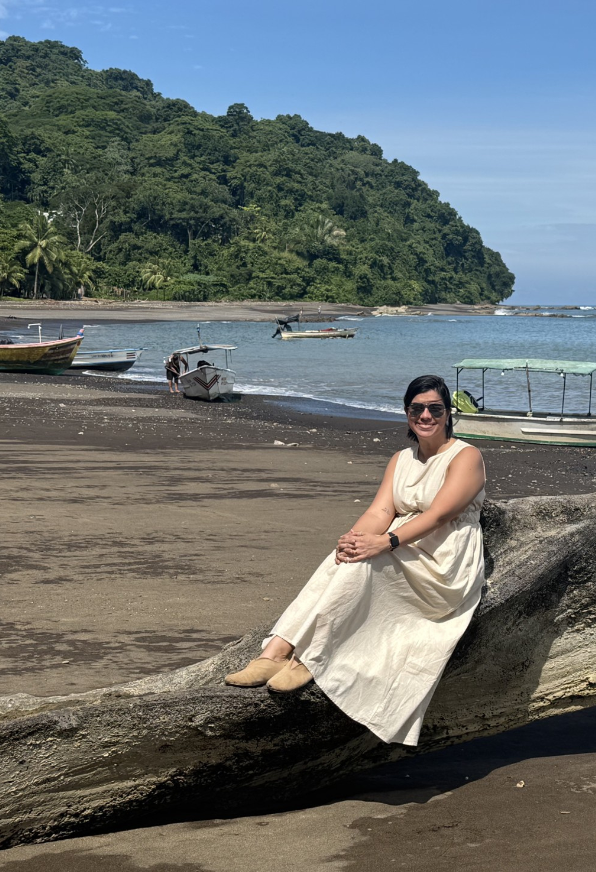 Woman wearing sunglasses and yellow top, smiling in front of a pink and white striped wall.