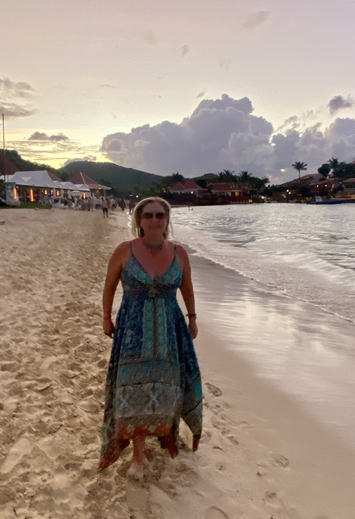 Woman in red dress and sunglasses, standing against a pink and white striped wall.