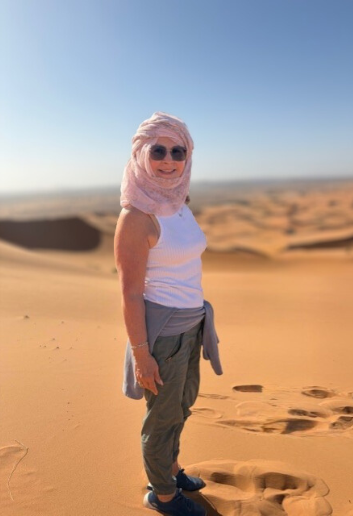 Woman on beach wearing a straw hat, sunglasses, and pink dress; ocean and mountains in background.