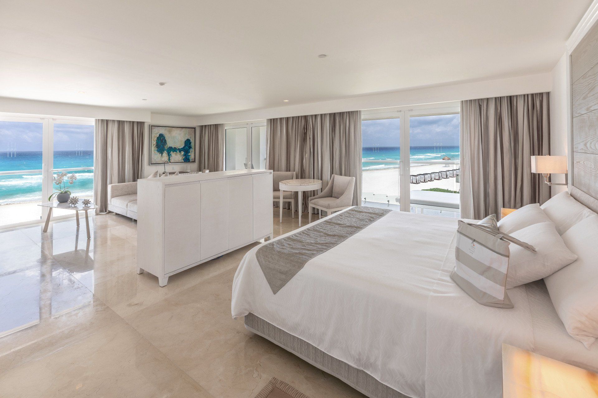 Bright hotel room with ocean view, large bed, white decor, beach.