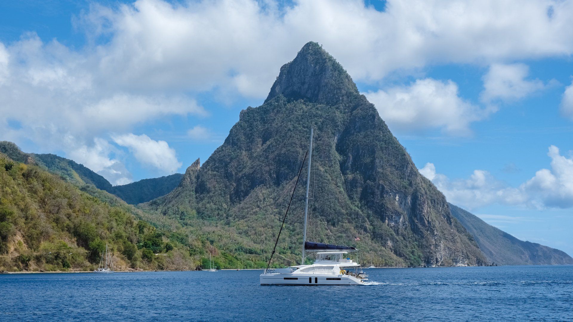 Sailboat on blue water with lush green mountains and Pitons under a cloudy sky.