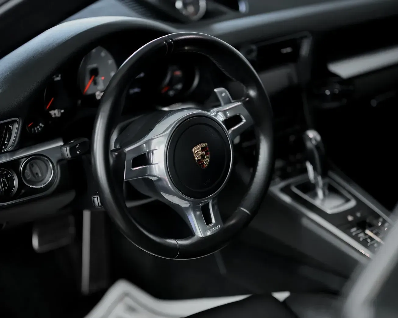 Black Porsche car interior with steering wheel and gear shift.