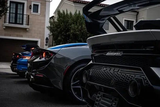 Three sports cars parked on a residential street: blue, gray, and black with spoilers.