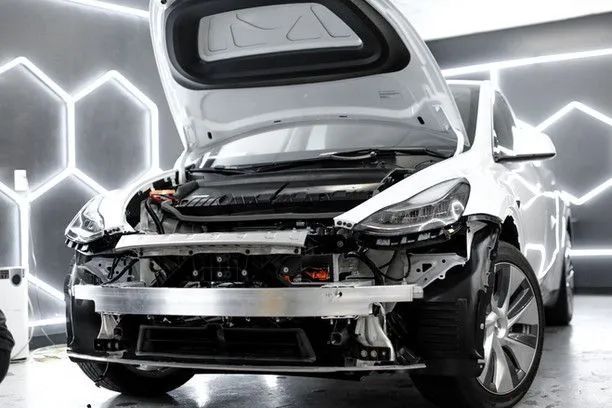 White Tesla car with open hood and trunk, undergoing repair in a garage with hexagon lights.
