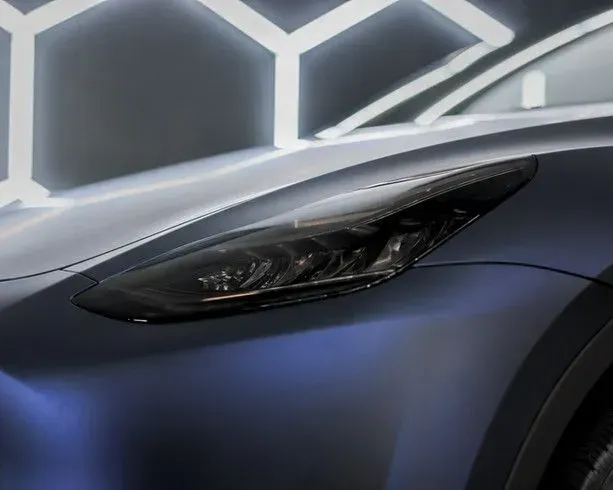 Close-up of a blue car's headlight, set against a dark background with hexagonal lighting.