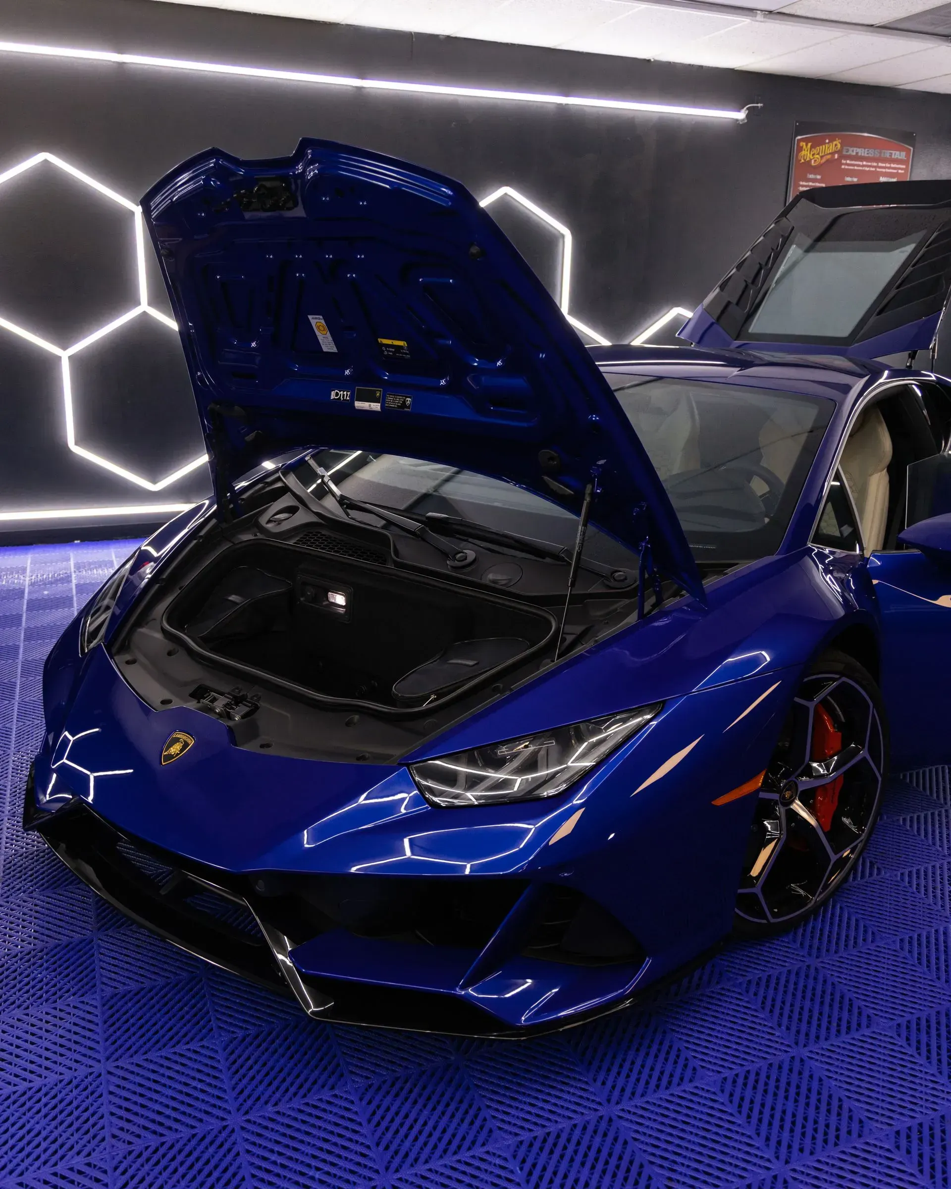 Blue Lamborghini with open hood and doors, in a showroom setting.