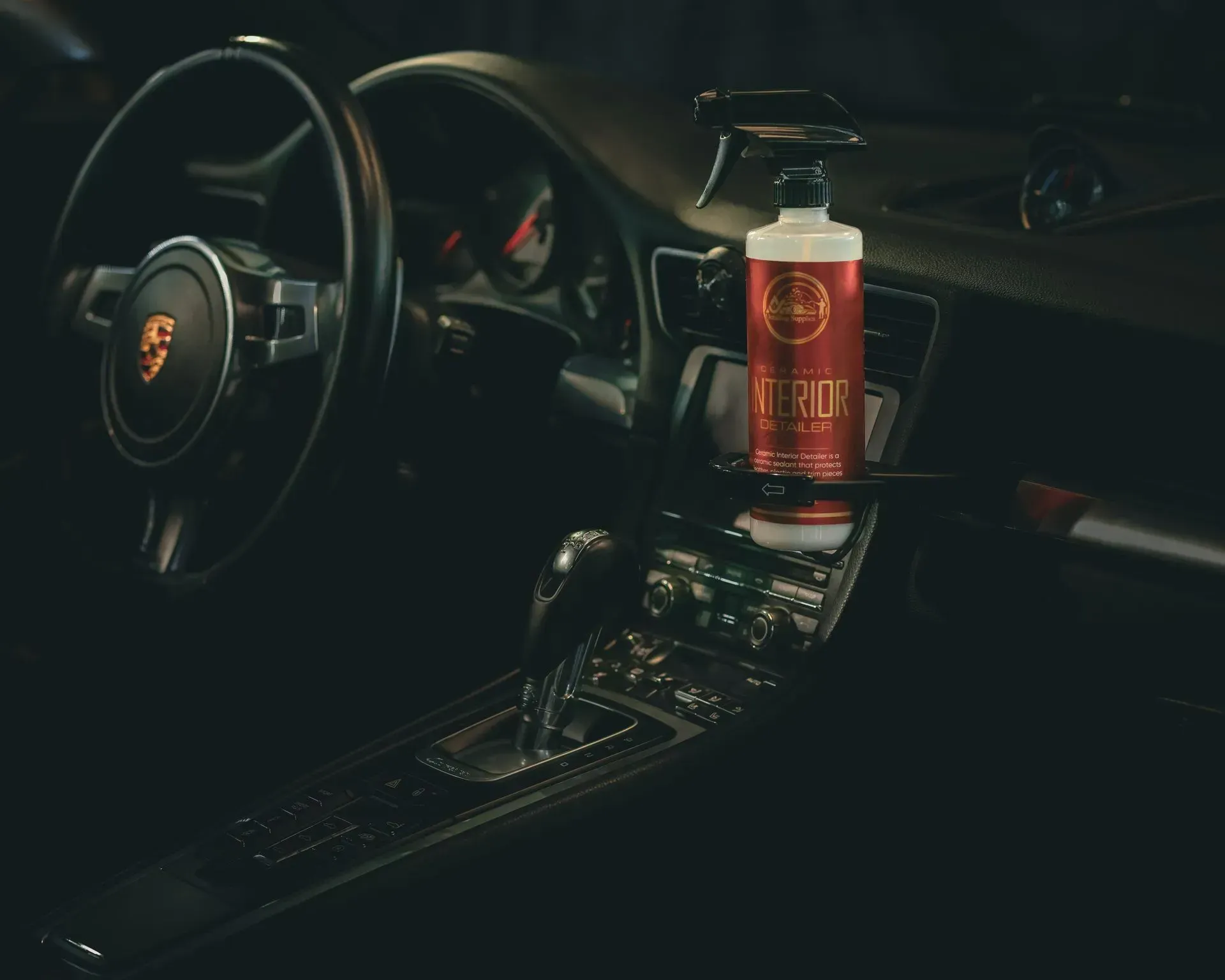 Car interior with a cleaning product bottle on the dashboard; a Porsche steering wheel and gear shift are visible.