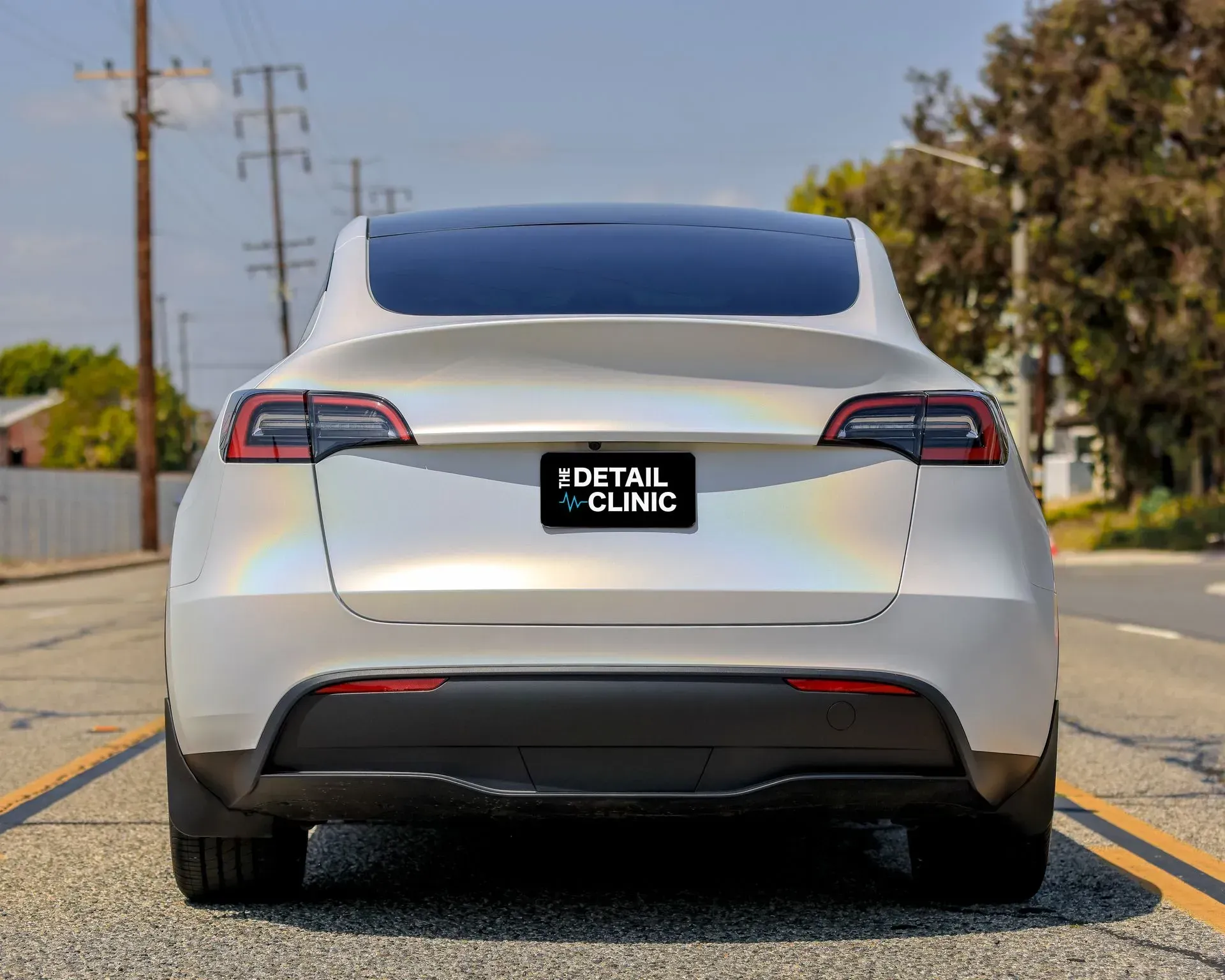 Rear view of a white Tesla with iridescent wrap on road, 