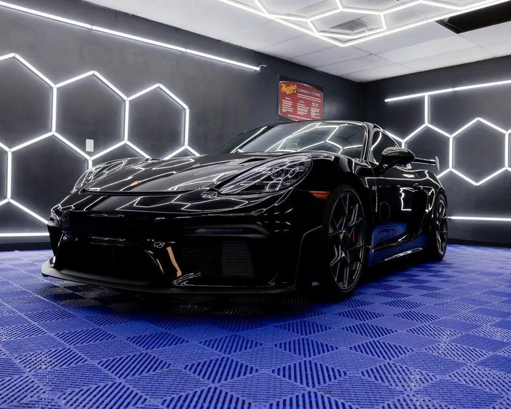Black sports car parked in a modern garage with hexagonal neon lights.