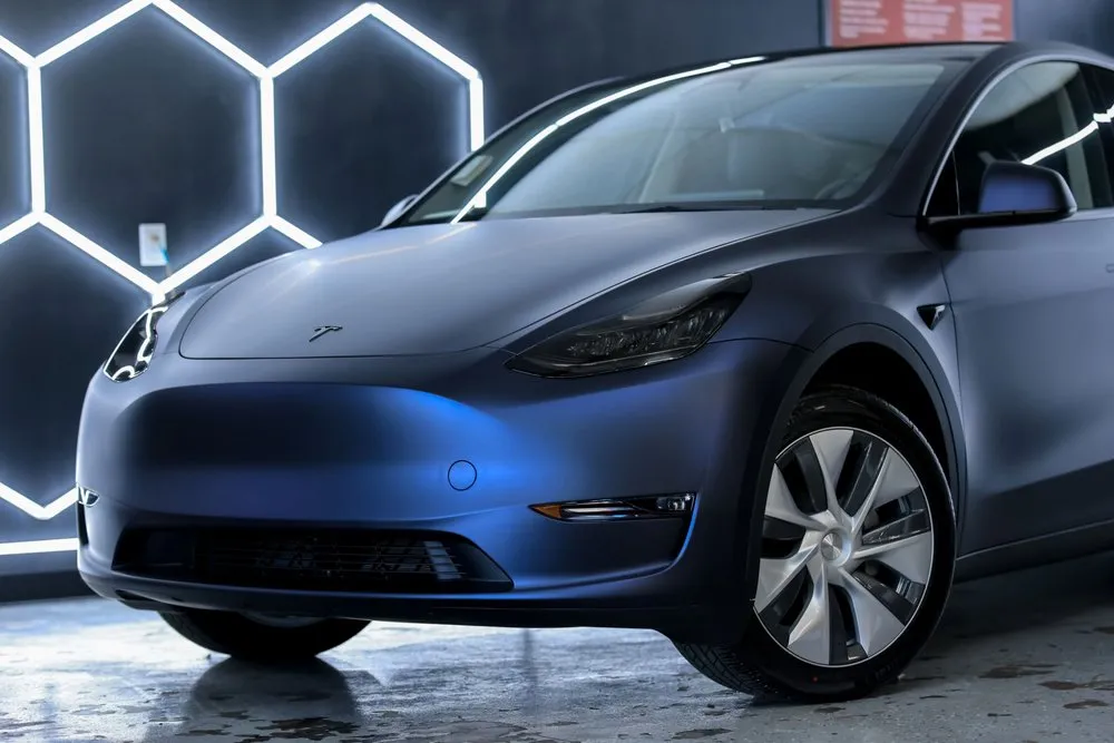 Blue Tesla Model Y, angled view, in a well-lit garage with hexagonal lights.