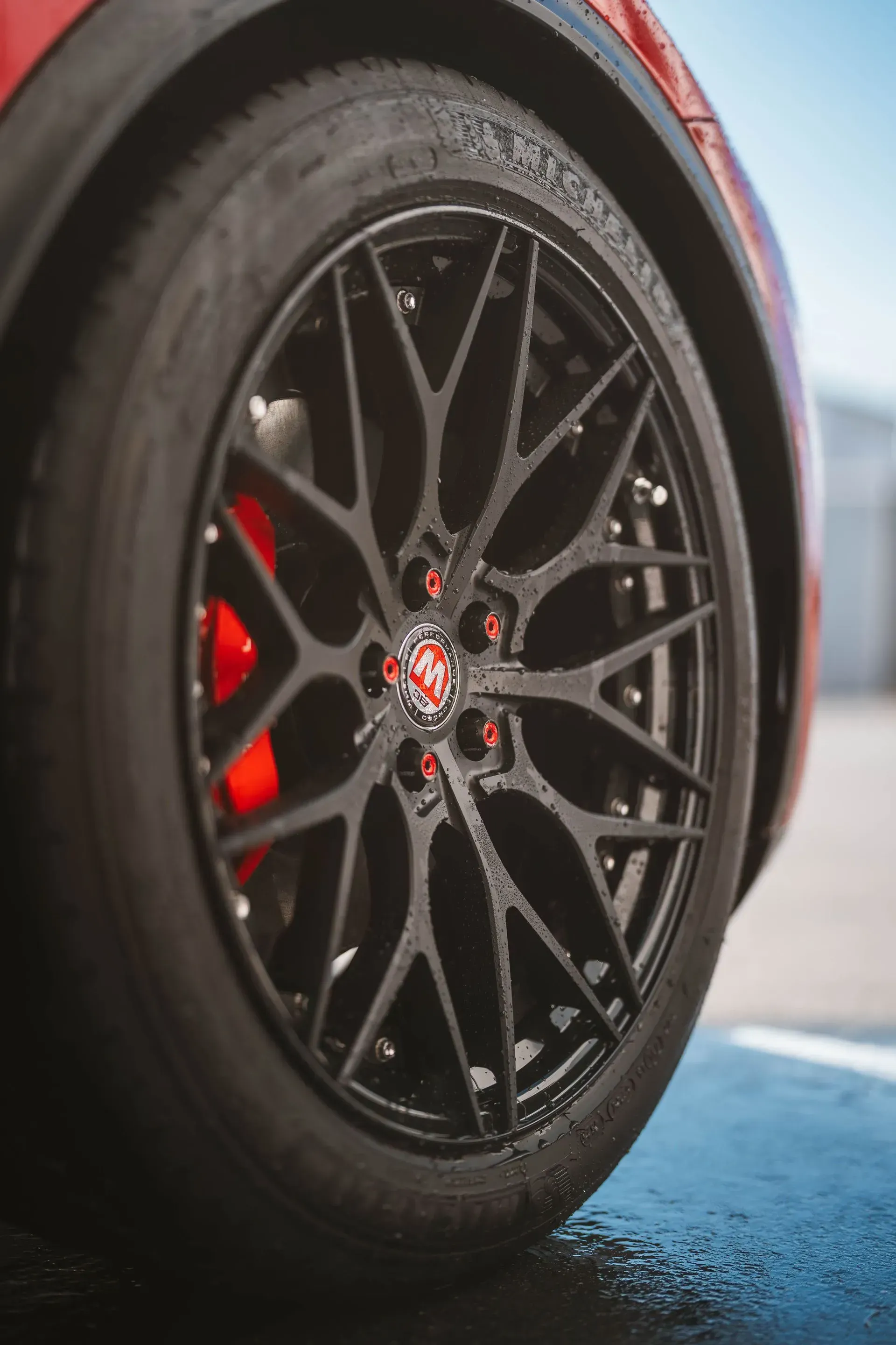 Black car wheel with red calipers and lug nuts.