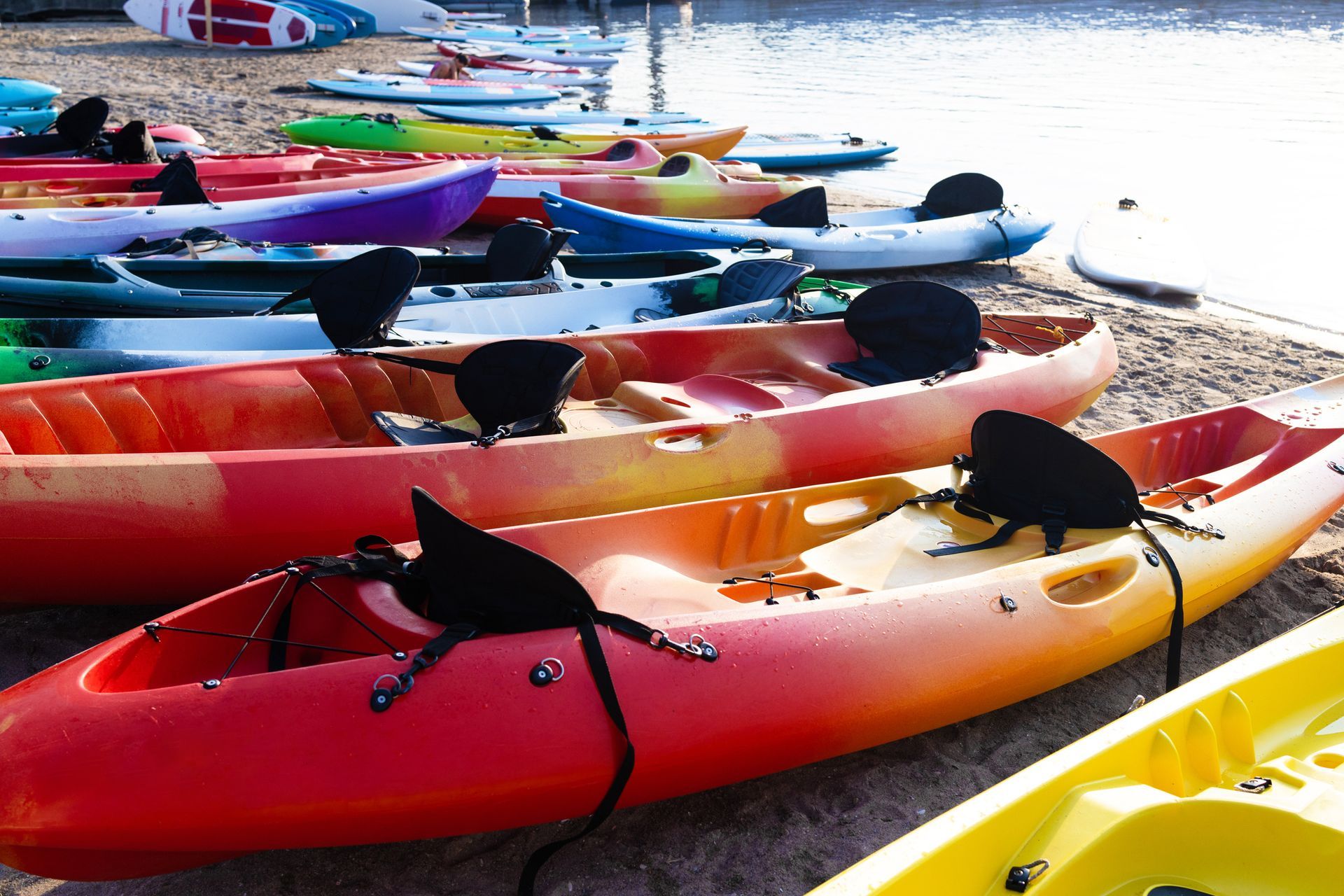 A bunch of kayaks are lined up on the beach near the water