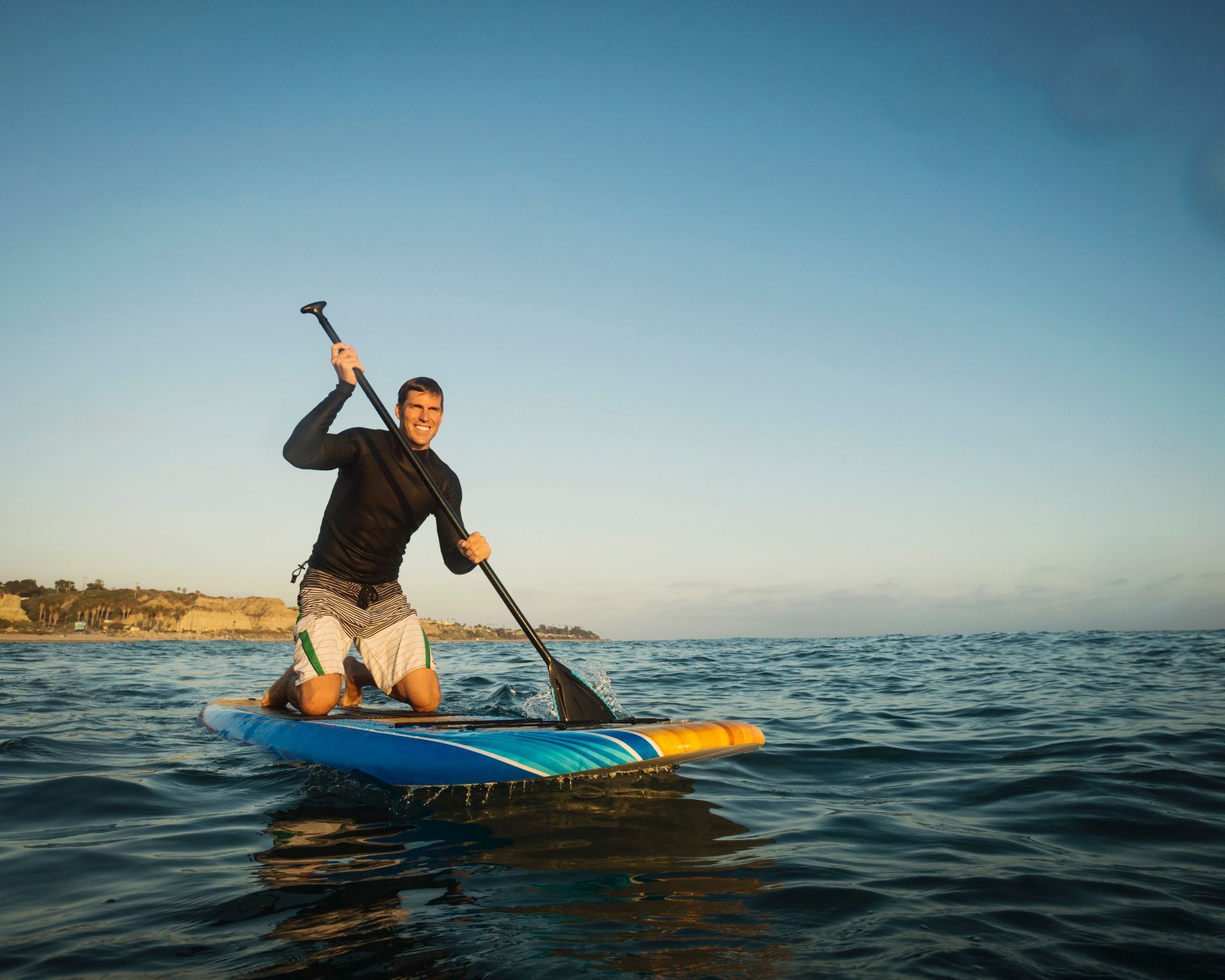A man is kneeling on a paddle board in the ocean.