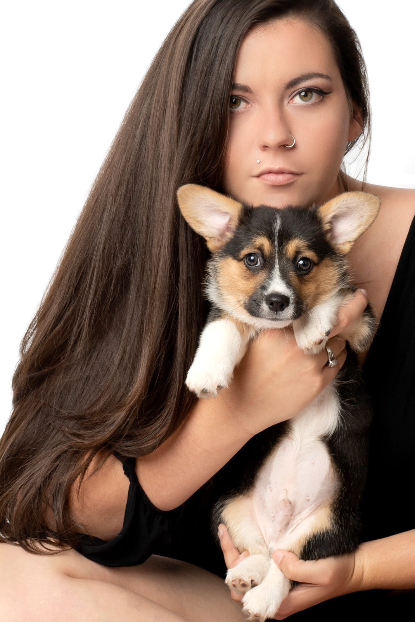 Woman with long brown hair holds a tri-color Pembroke Welsh Corgi puppy.
