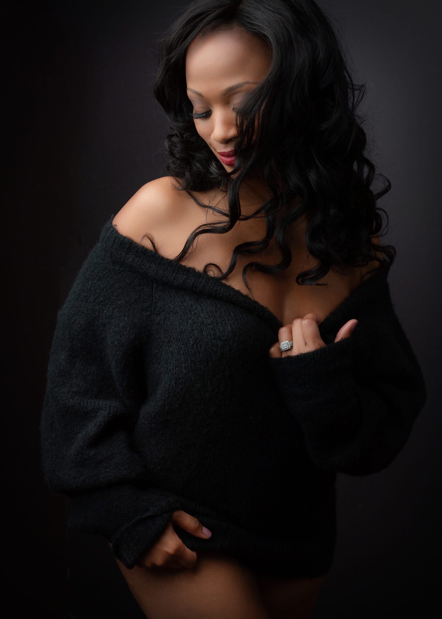 Woman in black sweater, eyes closed, hand on chest. Black hair, dark background.