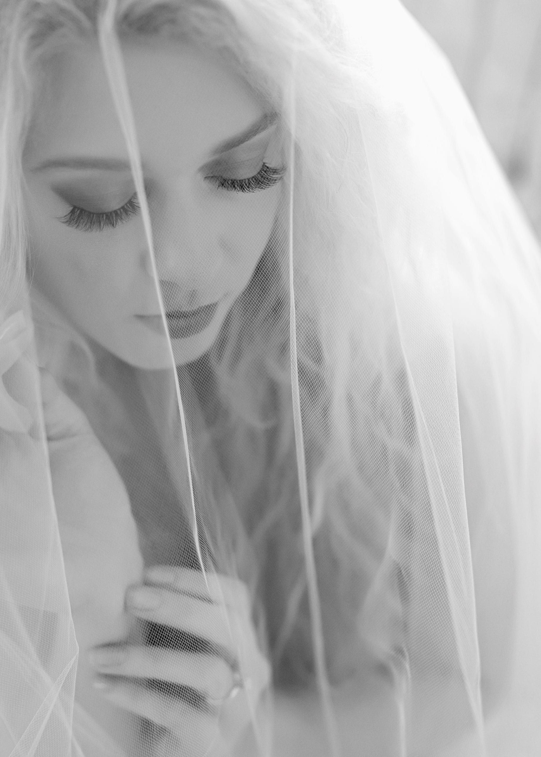 Blonde woman in a sheer veil, looking down. Black and white photo, soft focus.